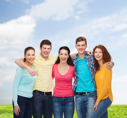 group of smiling teenagers over blue sky and grass