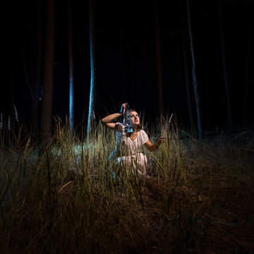 woman in nightgown sitting in high forest at night with lantern
