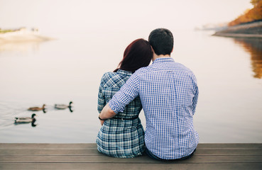 Rear view of a romantic young couple sitting on the river dock i