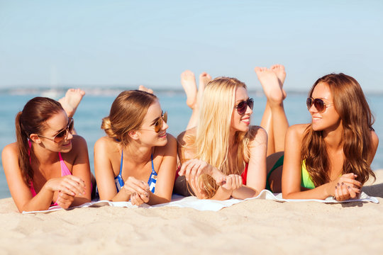group of smiling women in sunglasses on beach