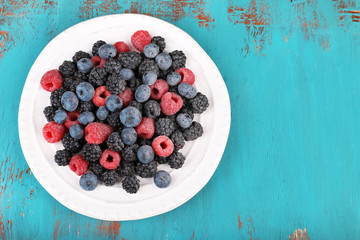 Iced berries on plate, on color wooden background