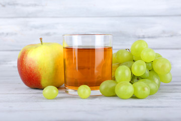 glass of juice with fresh grape and apple on grey wooden table