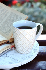 Cup with hot drink and book on bench, outdoors