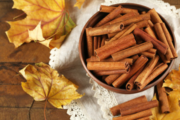 Cinnamon sticks in bowl with yellow leaves on wooden background