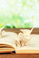 Origami cranes on old book on wooden table, outdoors