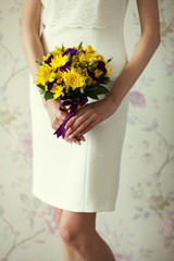 Bride's hands with wedding bouquet of violet and yellow flowers