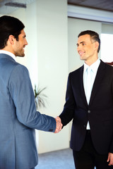 Fototapeta premium Two happy businessman shaking hands while standing in a hall