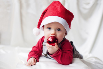 Funny baby in Santa Claus cap with a Christmas ball - obrazy, fototapety, plakaty
