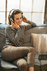 Obraz premium Happy young woman sitting on sofa and listening music