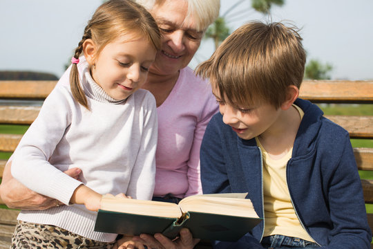 grgrandmother reading book to grandchildren outdoors