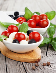 Fresh cherry tomatoes, mozzarella, olive and basil on old wooden