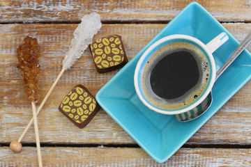 Black coffee, chocolates and sugar sticks on rustic wood