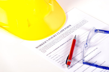 Worker injury claim hard hat with eyeglasses and pen on white