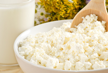 Cottage cheese in bowl with wooden spoon and milk