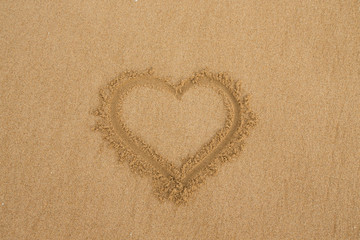 drawing a heart on wet golden beach sand