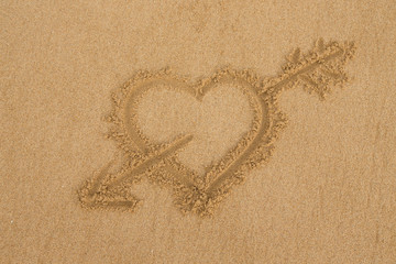 drawing a heart with an arrow on wet golden beach sand