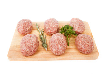 fresh uncooked patties on a wooden board with rosemary and parsl