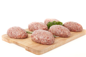 fresh uncooked patties on a wooden board with rosemary and parsl