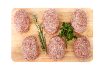 fresh uncooked patties on a wooden board with rosemary and parsl
