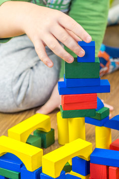 child is playing with multicolored cubes on wooden floor