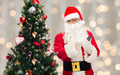 santa claus with smartphone and christmas tree