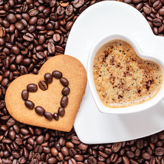Heart shaped cup and cookie on coffee beans background