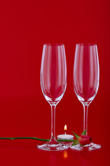 Two wine glasses with rose and candle over red