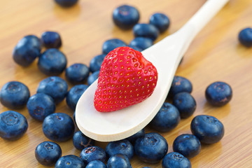 Strawberry on a wooden spoon with blueberries