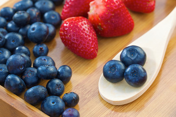 Blueberries on wooden spoon with strawberries