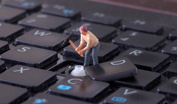 Miniature worker with pickaxe working on keyboard