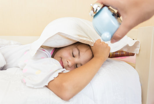 photo of mother holding alarm clock on sleeping daughters ear