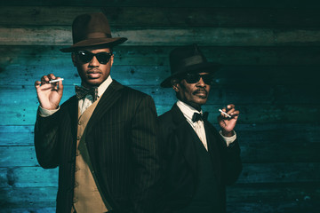 Two vintage african american gangsters smoking cigarette in fron