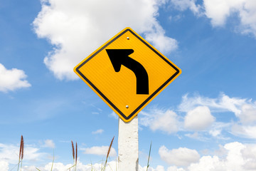 Left turn warning in farmland with cloudy blue sky background.