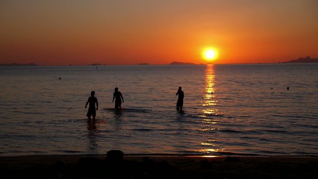 Silhouettes of Happy Young People Swimming in Sea against Sunset