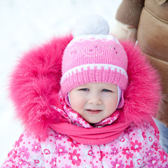 Funny cute baby girl with big blue eyes wearing a huge winter hat and a warm knitted jacket