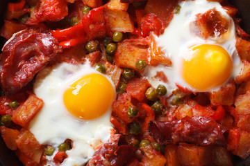 Fried eggs with chorizo, potatoes, peas and tomato close up