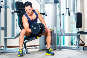 Fototapeta na wymiar Asian man lifting hand weight at gym