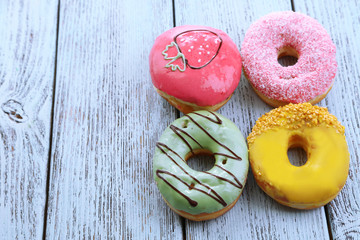 Delicious donuts with glaze on colorful wooden background