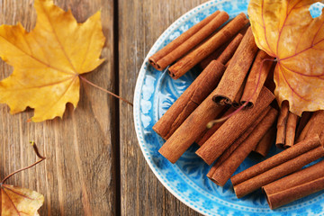 Cinnamon sticks on plate with yellow leaves on wooden
