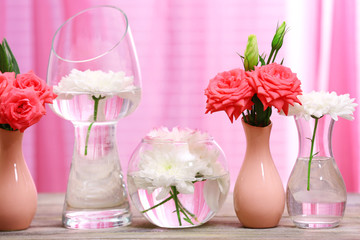 Beautiful flowers in vases on table on curtains background