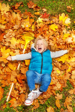 Boy laughing and laying on autumn leaves with rake