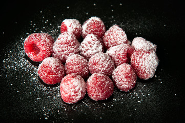 Beautiful raspberries with a sugar powder on a black background
