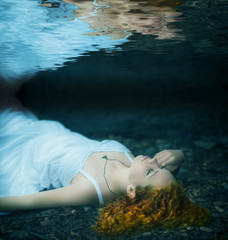 Young redhead beautiful woman lying underwater.