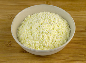 Bowl full of white milk powder against a wooden background
