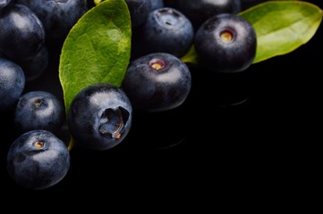 Several whole blueberries with leaves isolated on black corner
