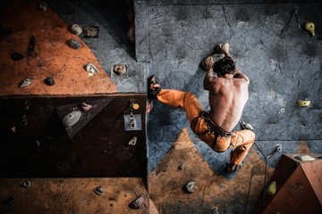 Muscular man practicing rock-climbing on a rock wall indoors - obrazy, fototapety, plakaty