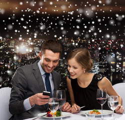 smiling couple with smartphone at restaurant