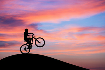 silhouetted mountainbiker doing wheelie in sunset sky on hill