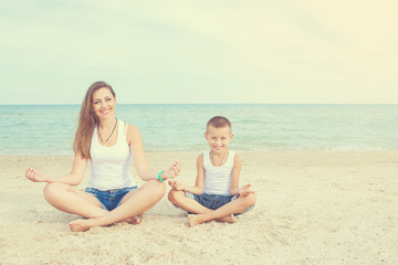 Mother and her son doing yoga on coast of sea on beach.