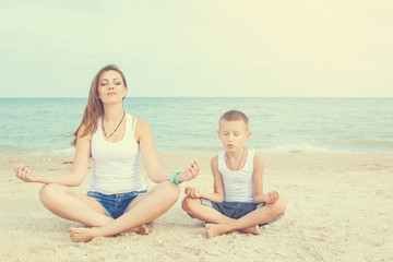 Mother and her son doing yoga on coast of sea on beach.